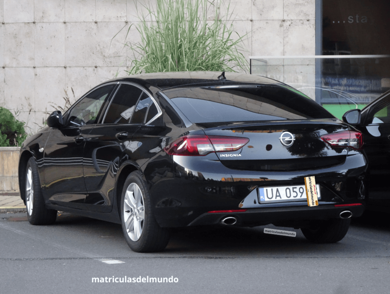 Sedán negro Opel Insignia con matrícula de vehículo militar del ejército de Polonia aparcado en frente de un edificio de losetas blancas
