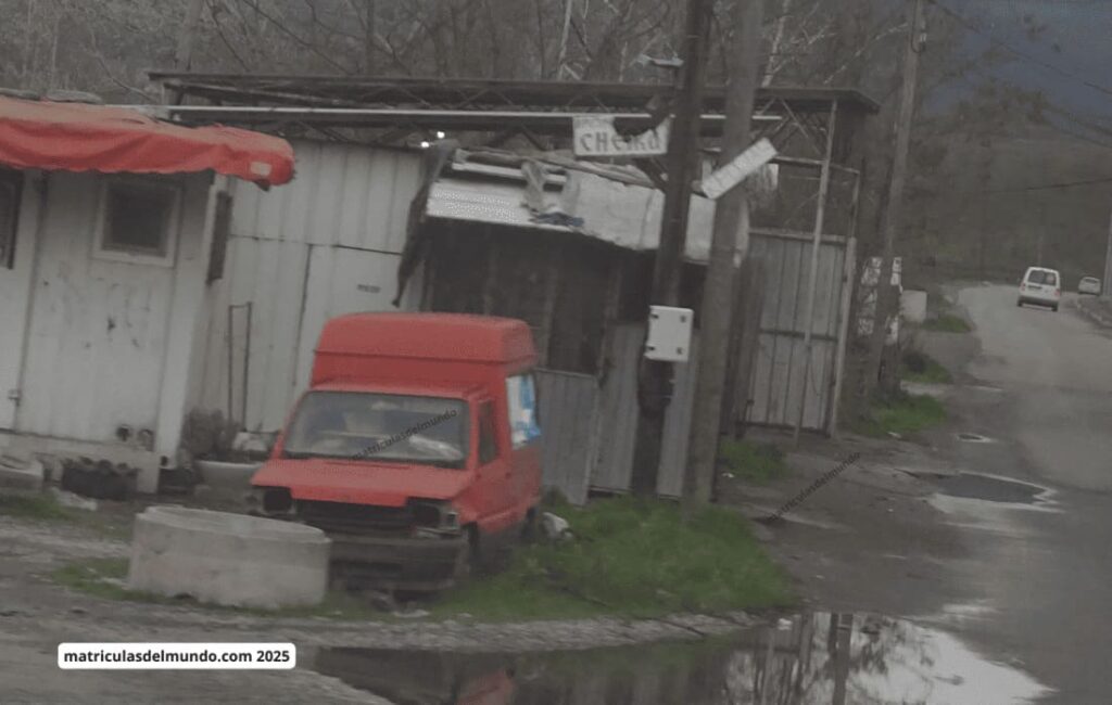 Furgoneta roja Seat Terra abandonada sin matrícula frente a una construcción precaria en Kosovo.